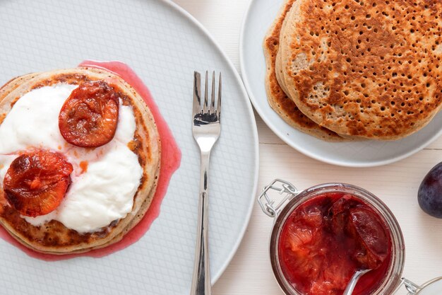 High angle close-up of banana crumpets with plum compote and creme fresh on white wooden table