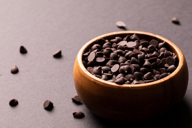 色付きの背景に木のボウルに入った新鮮なチョコレートチップの高角度のクローズアップビュー。変更されていない、甘い食べ物と不健康な食事のコンセプト。