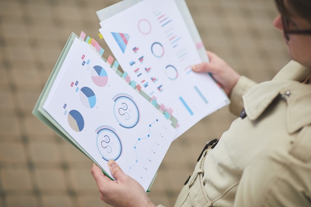 High angle close up of young businessman holding documents with charts and graphs while standing outdoors in autumn, copy space