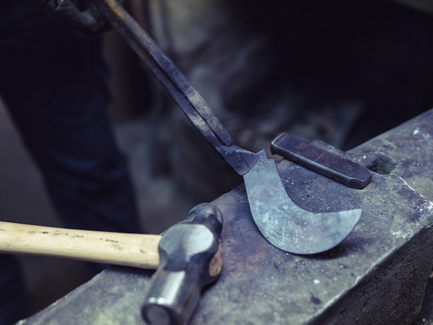 High angle of crop anonymous male farrier demonstrating metal piece placed on anvil in shabby smithy