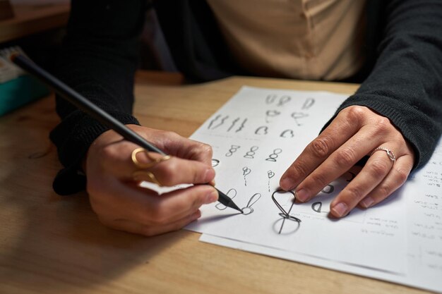 High angle of crop unrecognizable jeweler creating pictures of rings with pencil on paper sheet on wooden table