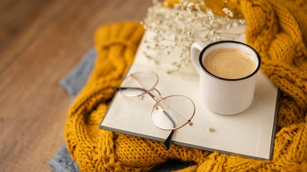 High angle of cup of coffee on book with glasses and sweaters