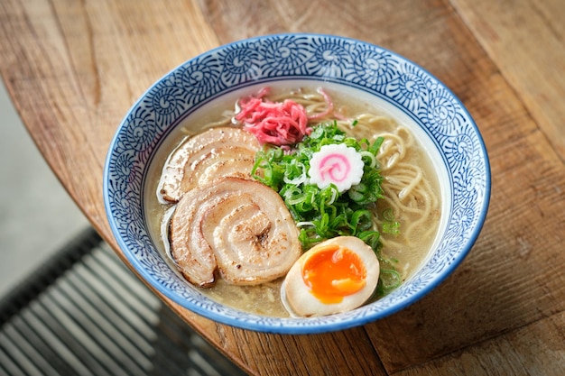 木製テーブルの上の陶器のボウルに麺と肉が入ったおいしい日本のスープの高い角度