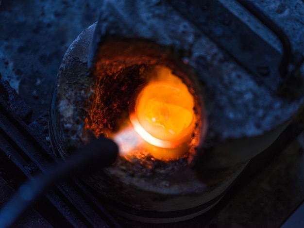 높은 각도의 불타는 금속을 어두운 용광로에 넣고 가스 토치로 녹입니다.