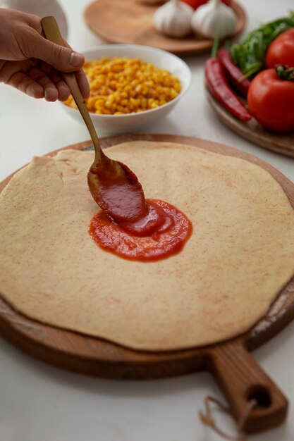 Mano ad alto angolo che mette la salsa sull'impasto della pizza