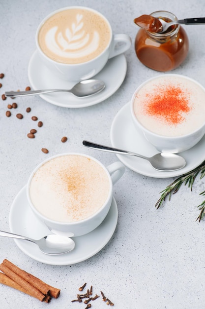 High angle image of cappuccino with cream and spices in three\
cups on saucers