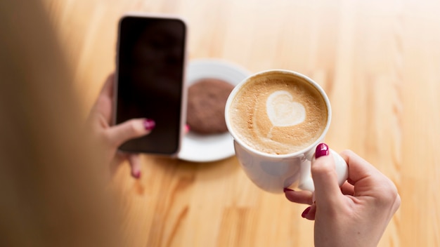 写真 スマートフォンを押しながらコーヒーを飲んでいる女性のハイアングル