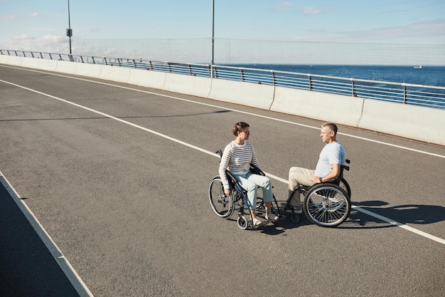 屋外でチャットし、都市生活を楽しんでいる車椅子の大人のカップルのハイアングルの肖像画