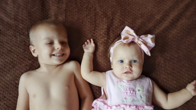 Photo high angle portrait of baby girl with shirtless brother lying on bed