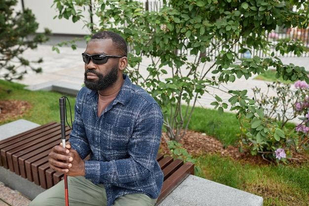 Photo high angle portrait of blind man wearing sunglasses and holding cane in braille while sitting on ben