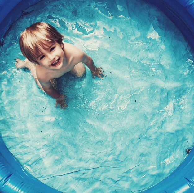 Высокоугольный портрет милого мальчика, играющего в надувном бассейне