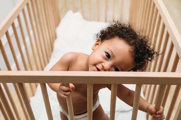 high angle portrait of cute shirtless baby boy standing in crib at home
