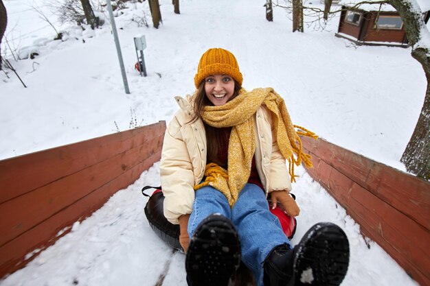 High angle portrait of excited young woman sledding downhill in winter enjoying fun outdoor activiti