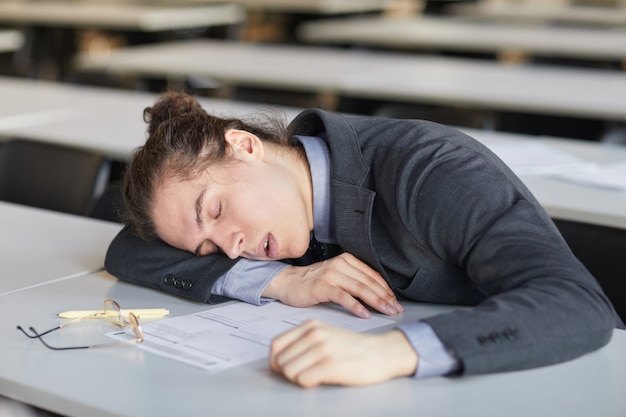 Ritratto ad alto angolo di un giovane esausto che dorme alla scrivania a scuola mentre sostiene gli esami, copia spazio