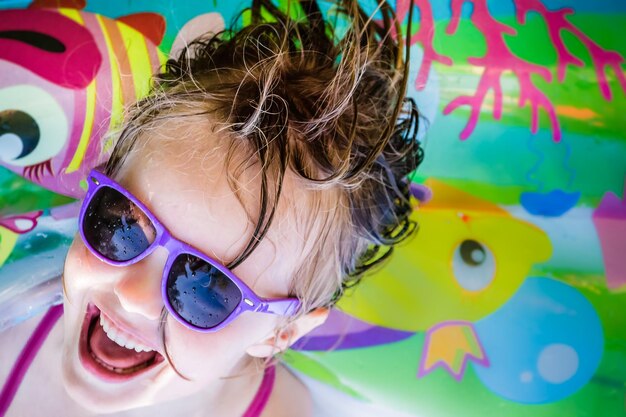 Foto ritratto ad alto angolo di una ragazza che indossa occhiali da sole con bambini colorati che giocano a biliardo sullo sfondo
