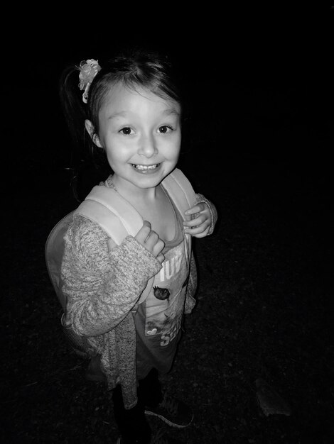 High angle portrait of happy girl with backpack standing on field at night