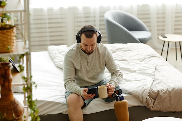 High angle portrait of man with prosthetic leg enjoying morning at home and listening to music with
