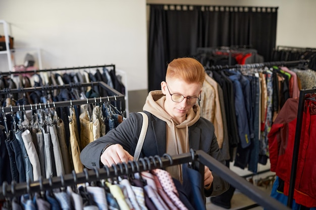 Высокоугольный портрет рыжеволосого молодого человека, смотрящего на одежду во время покупок.