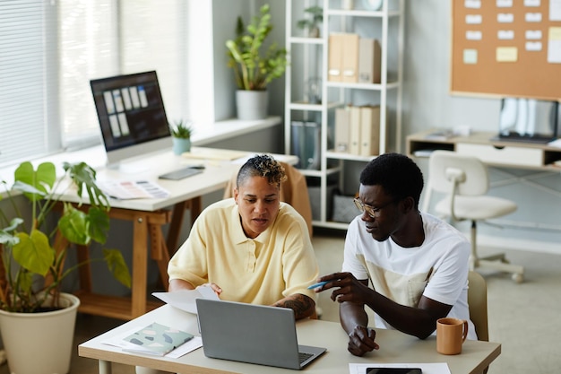 High angle portrait of two african american business people using laptop together in it office and w