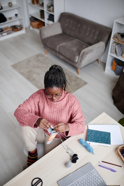 High angle portrait of young africanamerican woman knitting at home in cozy room copy space