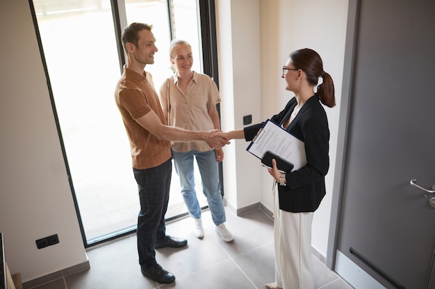 Photo high angle portrait of young couple shaking hands with real estate agent during apartment tour, copy space