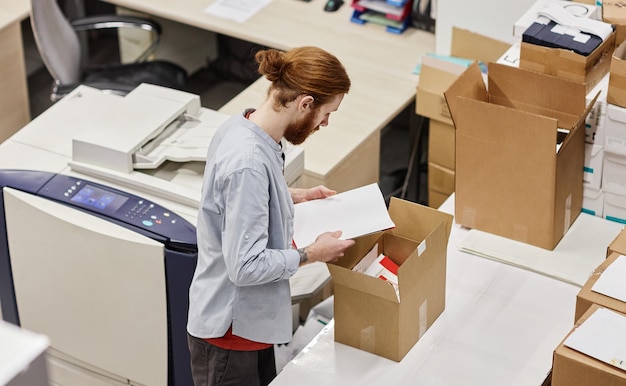 High angle portrait of young man packaging print products in\
publishing shop copy space