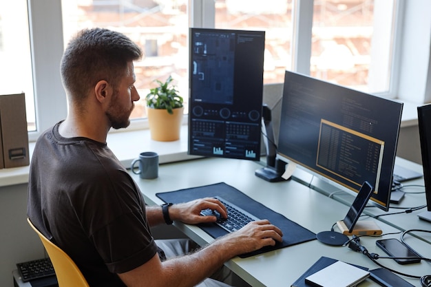 High angle portrait of young software engineer writing code at workplace with multiple computer scre