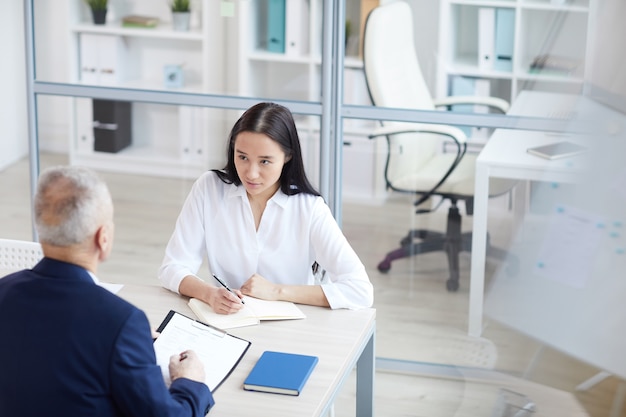 High angle portrait of young woman answering questions during job interview in office