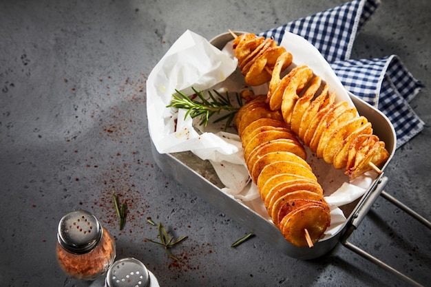 High angle shot of delicious twist potatoes on skewers served with pepper and napkin on a gray table