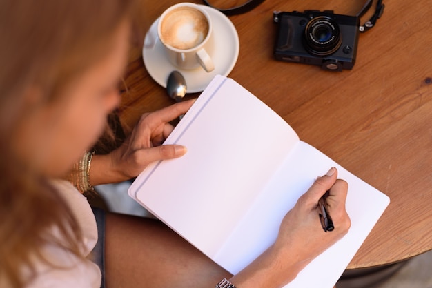 Foto colpo di alto angolo di una donna che scrive in un taccuino e che beve caffè