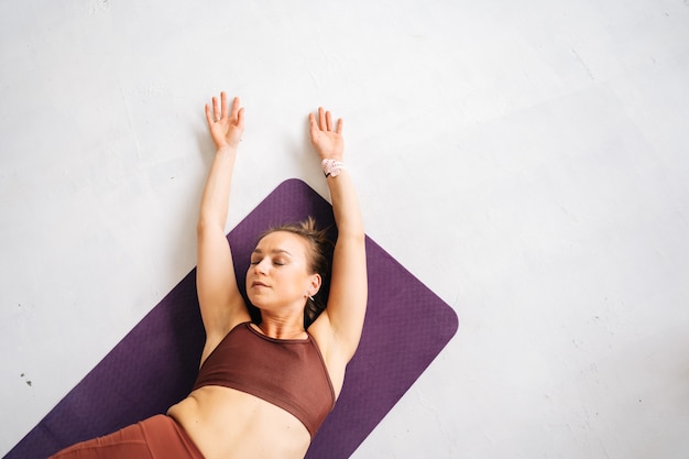 High-angle shot of fit young woman with perfect athletic body wearing sportswear working out lying on exercising mat. Concept of healthy lifestyle and physical activity at home.