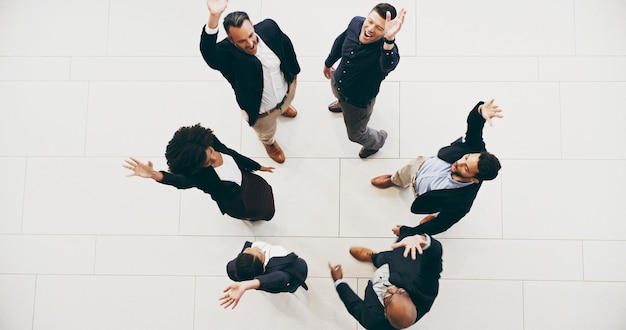 High angle shot of a group of businesspeople raising their hands in triumph in a modern office