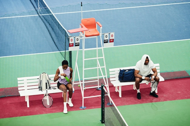 High angle shot of two tennis players relaxing on bench while taking break from match or practice in