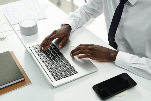 High angle view of african american businessman sitting at table and typing on laptop during her wor