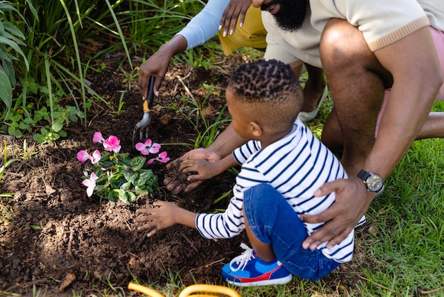 アフリカ系アメリカ人の母親と父親と息子が土の中に新鮮な花を植えている様子を高い角度から見た図。変更されていない、ライフスタイル、ガーデニング、家族、愛、一体性、週末、自然、子供時代のコンセプト。