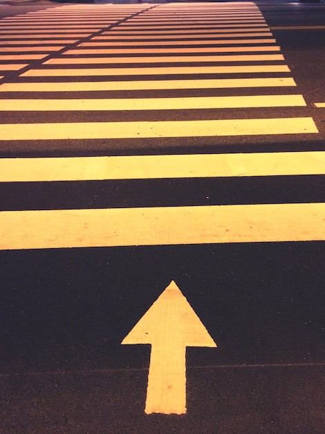 Photo high angle view of arrow sign leading towards zebra crossing on road at night