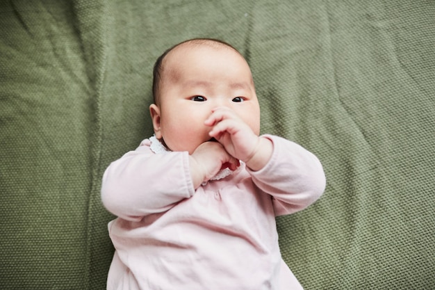 침대에 누워 손가락을 가지고 노는 귀여운 아시아 아기의 높은 각도