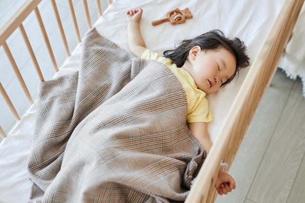 Вид под высоким углом на азиатскую девочку, спящую в своей кроватке дома