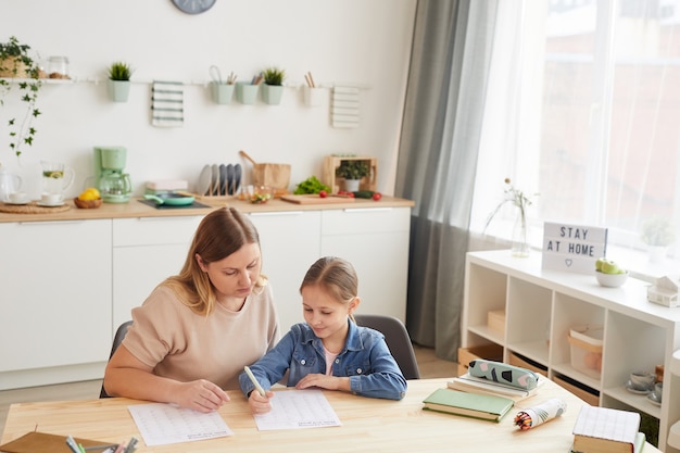 写真 宿題をしているかわいい女の子を助け、居心地の良いインテリア、コピースペースで自宅で勉強している思いやりのある母親のハイアングルビュー