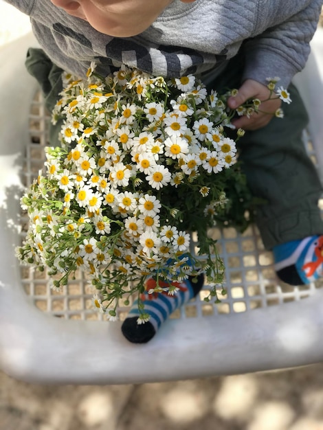 Foto vista ad alto angolo di un bambino con un bouquet di fiori seduto nel cesto
