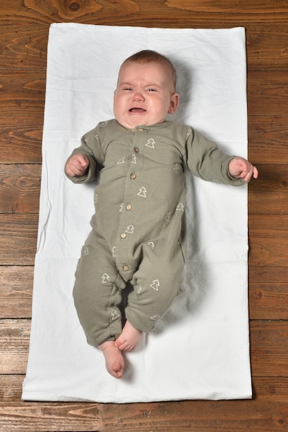 High angle view of a baby on the parquet floor dressed, crying and looking at the camera