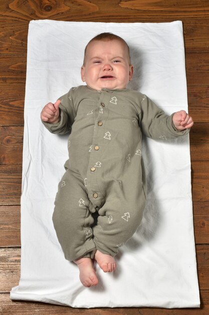 High angle view of a baby on the parquet floor dressed, crying and looking at the camera