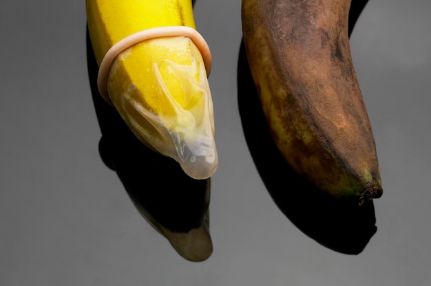 Высокоугольный вид бананов с презервативом на сером фоне
