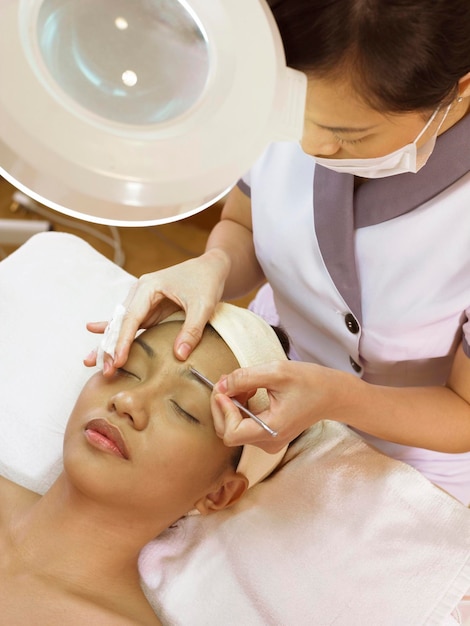 High angle view of beautician giving beauty treatment to woman lying on bed