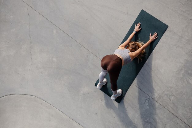 High angle view of the beautiful young woman training outside\
while standing at the yoga mat