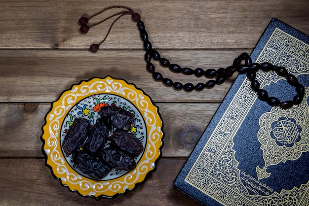 High angle view of book with rosary beads and dates on wooden table