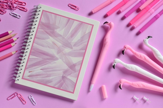 High angle view of books with pens and paper clips on pink background