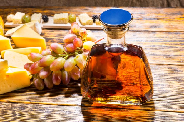 High Angle View of Bottle of Whiskey Alcohol on Rustic Wooden Table with Variety of Cheeses and Grapes with Copy Space