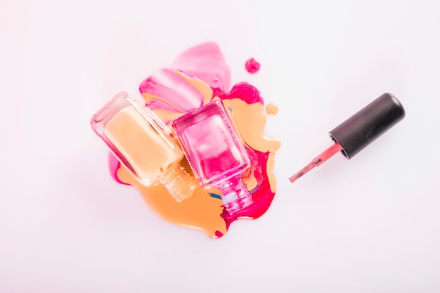 High angle view of bottles with spilled nail polish on pink backdrop