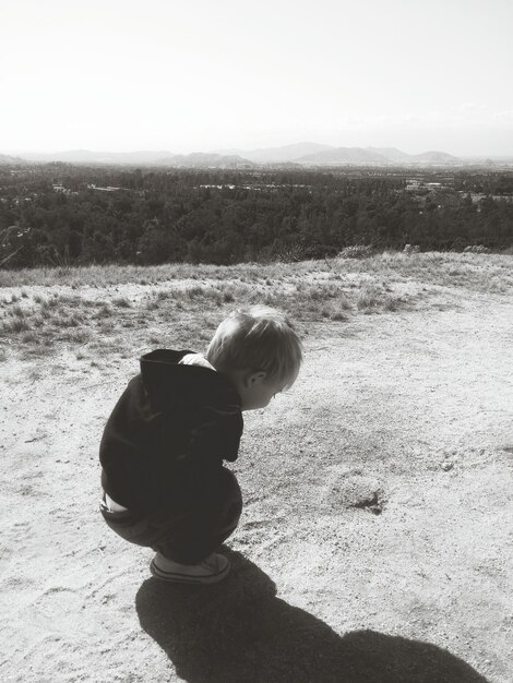 Foto vista ad alta angolazione di un ragazzo che guarda un insetto sul campo contro un cielo limpido